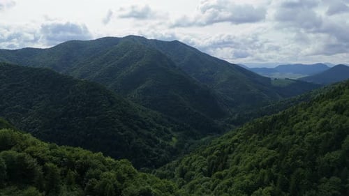 Aerial View of Green Mountain Valley with Forest Hills and Distant Peaks Under Clouds