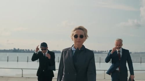 Confident Business Leaders Walking by Waterfront under Cloudy Sky