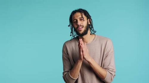 Man with Dreadlocks Gesturing in Front of Blue Background