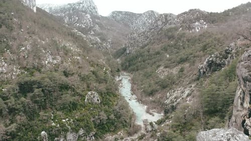 Flug durch eine Schlucht mit blauem Wasser zwischen Bergen und Bäumen im Winter