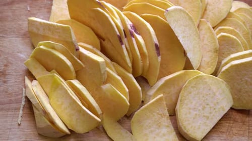Raw Sweet Potatoes Cut In Slices On Wooden Chopping Board. overhead panning right