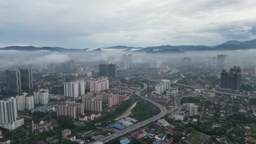 Cityscape of Kuala Lumpur beneath soft blanket of low fog and clouds.
