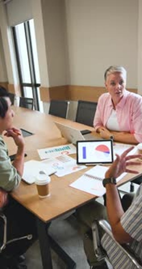 Vertical video: Diverse coworkers initiating chart review at meeting table, pointing at pie chart