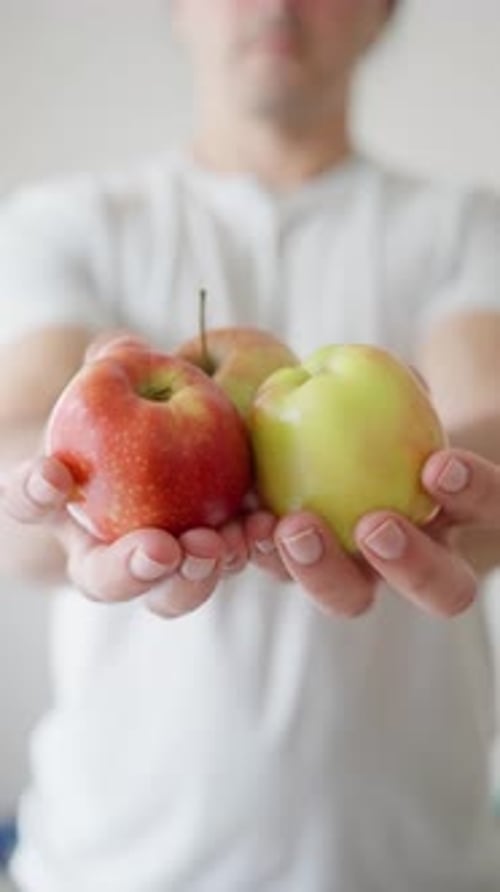 A Person Confidently Holding a Vibrant Mix of Red and Green Apples in a Sunny Setting