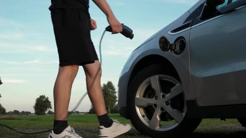 Man Charging Electric Vehicle on Rural Road