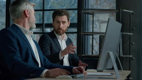 Two Caucasian Men Professional Businessmen Work Together Using Computer in Office Discussing