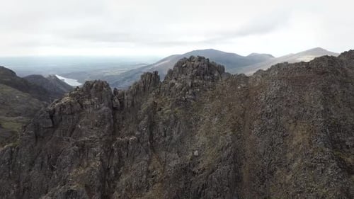 Drone shot of jagged mountain peaks rising above valleys under cloudy sky