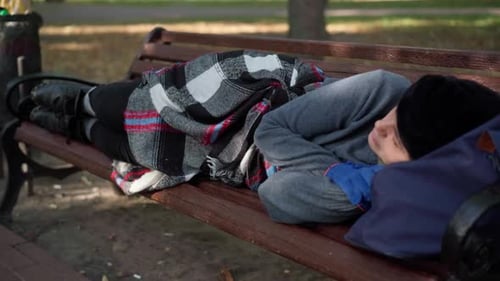 Young Homeless Woman Sleeping Lying on Bench in Urban City Park