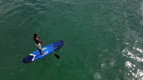 Aerial drone bird's eye view of Asian man exercising on a sup paddle board in turquoise tropical cle