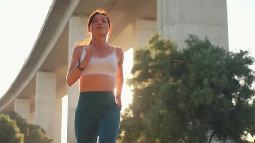 Sporty Woman Jogger Running Under Bridge During Bright Sunny Day