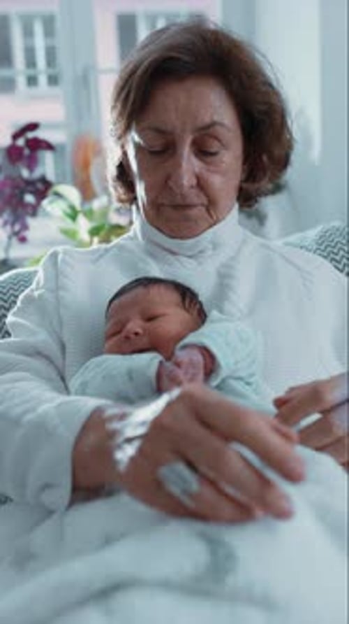 Senior Woman Holding Newborn Grandchild Inside Home