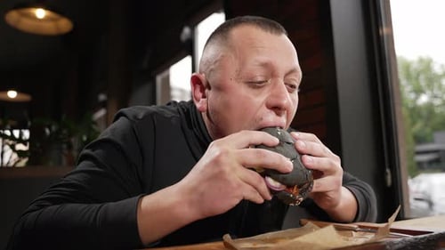 A Man Enjoys the Taste of a Burger While Sitting in a Cafe