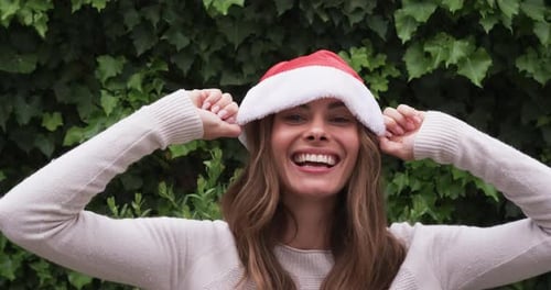 Woman Wearing Santa Hat Smiling in Front of Greenery