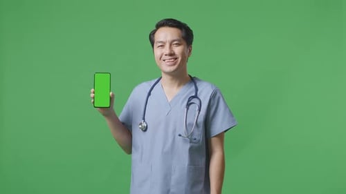 Asian Male Doctor With Stethoscope Smiling And Showing Green Screen Smartphone On Green Screen