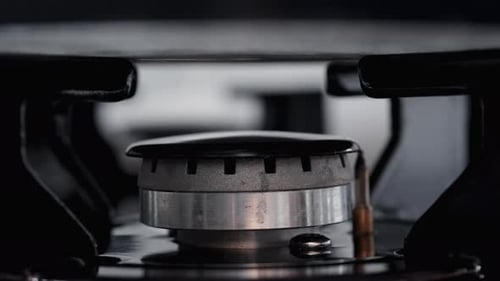 Close-up shot of a clean gas burner on a black stove with a pot placed on it, and the fire ignites.