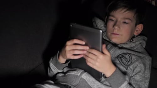 Boy Using Tablet Device Reclining on Couch At Night