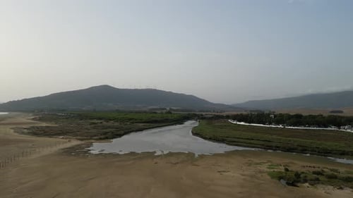Flying over beach towards river and forests with mountains in the background