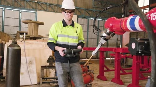 Weißer Ingenieur testet und steuert den Roboterarm in einer Fabrik für mechanische Fertigung.