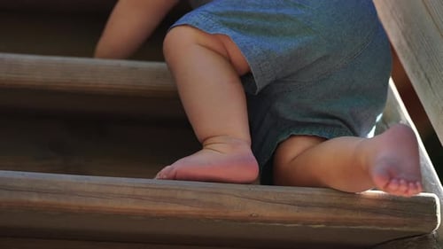 Barefoot toddler climbing upward on wooden playground ladder with small steady steps capturing
