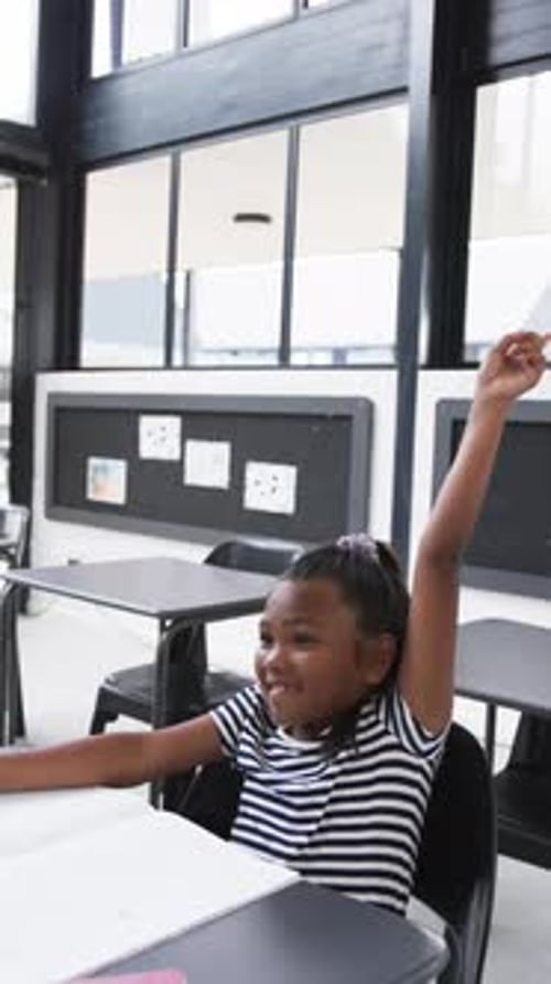 Vertical video: In a school setting, an African American young girl raises her hand