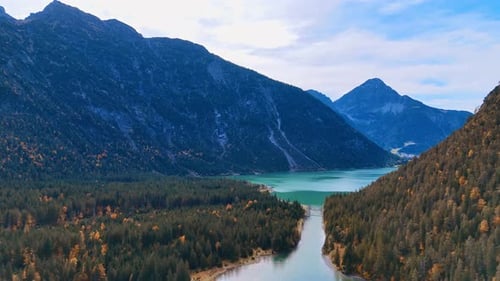 Flight above the pine tree forest growing around the beautiful lake with turquoise water.