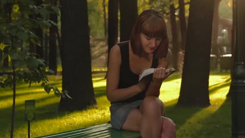Beautiful girl reads a interesting book and sitting at the city park