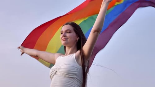 Woman Holding Rainbow Flag Against Bright Sky