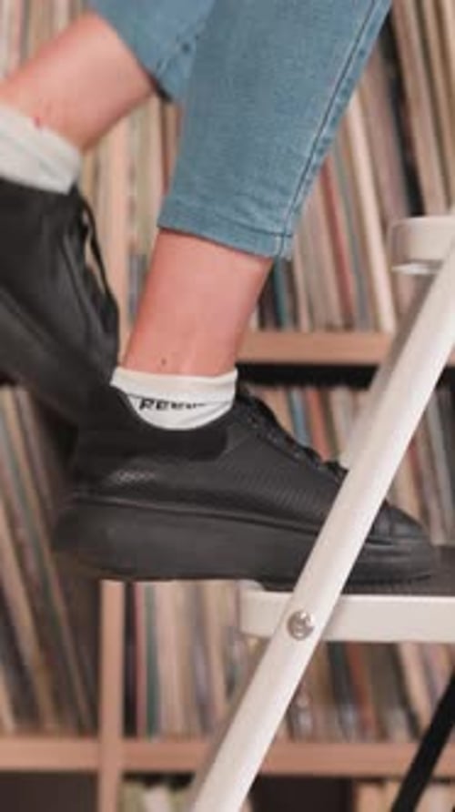 Woman Goes Up Step Ladder Near Bookcase
