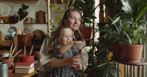Young Mother and Her Adorable Daughter Watering Flowers in the Home Garden