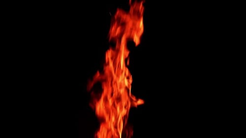 Long and thin flame of the fire burning in the darkness isolated. Tiny sparkles rise up in the air.