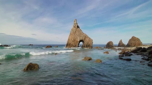 Static shot of a wild pebble beach with sharp cliffs and a natural rock arch in the Cantabrian Sea i