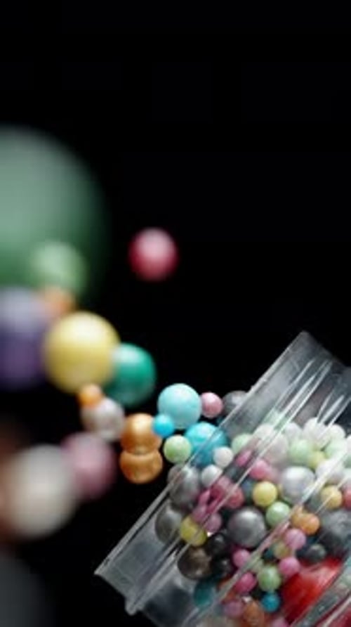 Vertical video. A Confectioner Pours Sweet, Colorful Sugar Balls of Different Sizes from a Container