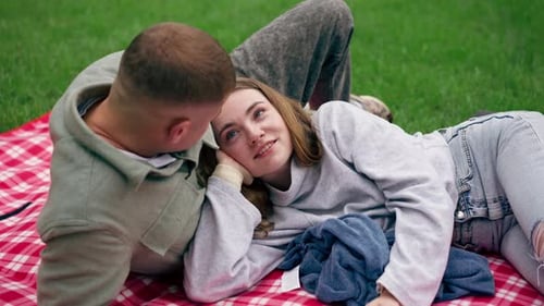 Close Up In the Park a Guy and a Girl in Warm Clothes are Resting on a Checkered Blanket Covered