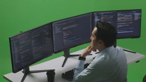 Side View Of Asian Man Thinking While Write Code With Multiple Computer Screens In Green Screen