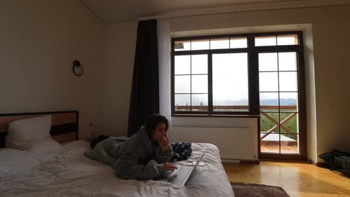 Junge Frau arbeitet am Laptop, während sie auf dem Bett liegt