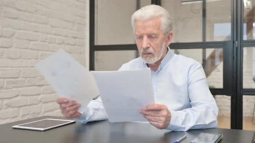 Senior Man Cheering After Reading Documents at Desk