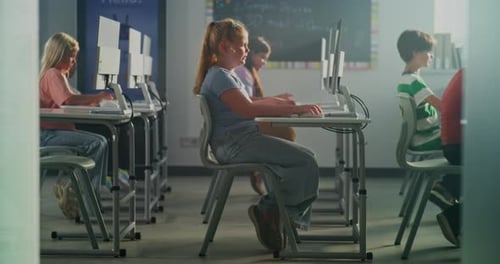 Blonde Schoolgirl Works Intently on Keyboard in Sunshine Classroom