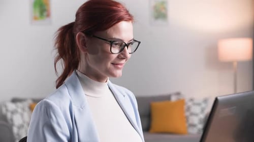 Portrait of Young Female Employee Working Remotely Behind a Laptop at Home Smiling and Looking at