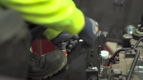 Mechanic tightens a nut on a bolt in a vice alongside colleague