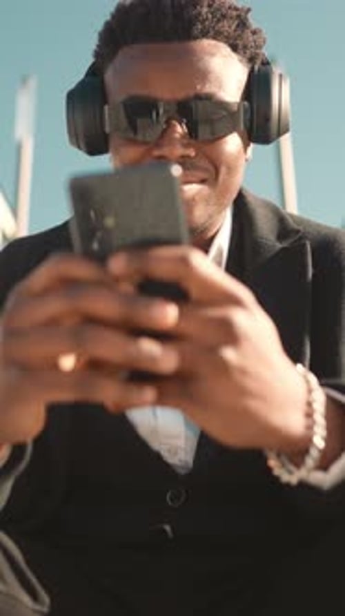 Young Adult Using Smartphone Wearing Headphones and Sunglasses
