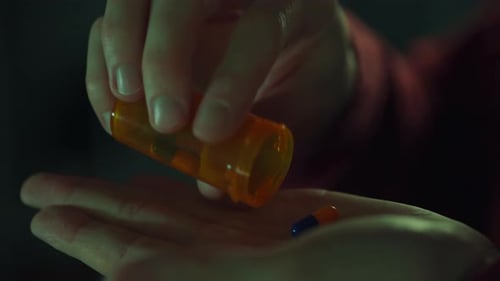 An orange bottle of pills in the hands of a young man. Close-up of male hands extracting