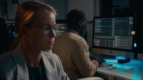 Two People Coding at Computers in Dark Office