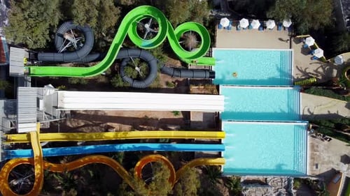 Drone hovers in a bird's eye view over a water park with slides - people slide down the tube slides