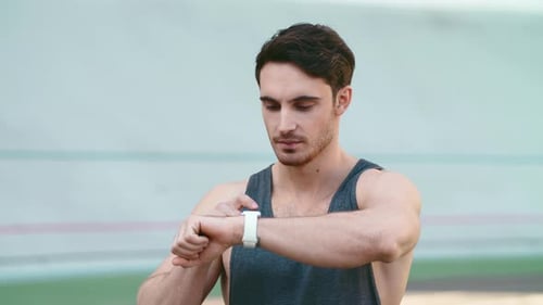 Handsome sport man checks smartwatch after workout at modern stadium track