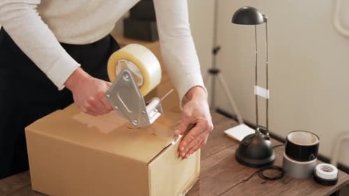 close-up of a man's hand packing a cardboard box with a packing gun