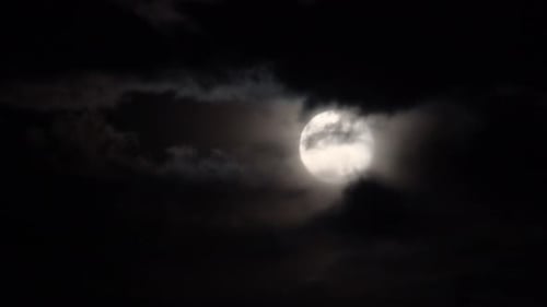 Vollmond mit gruseligen Wolken, die in einer dunklen Nacht vor uns vorbeiziehen.