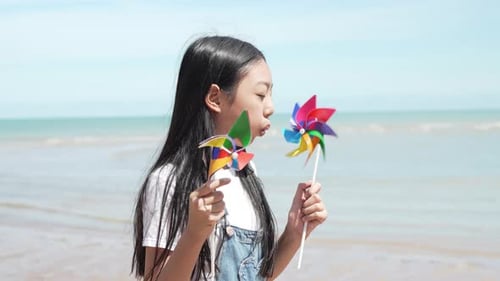 Smiling of little asian girl playing windmills outside on the beach together having fun