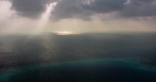 Rippled and calm sea with far mountains/islands on the horizon, rainy clouds and ray of sunlight r