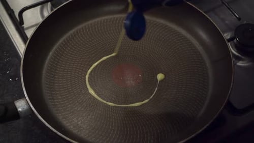 Flavored oil from squeeze bottle squirts into hot fry pan on stovetop