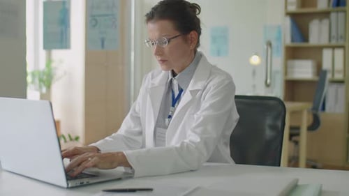 Female Doctor Typing on Laptop at Office Desk